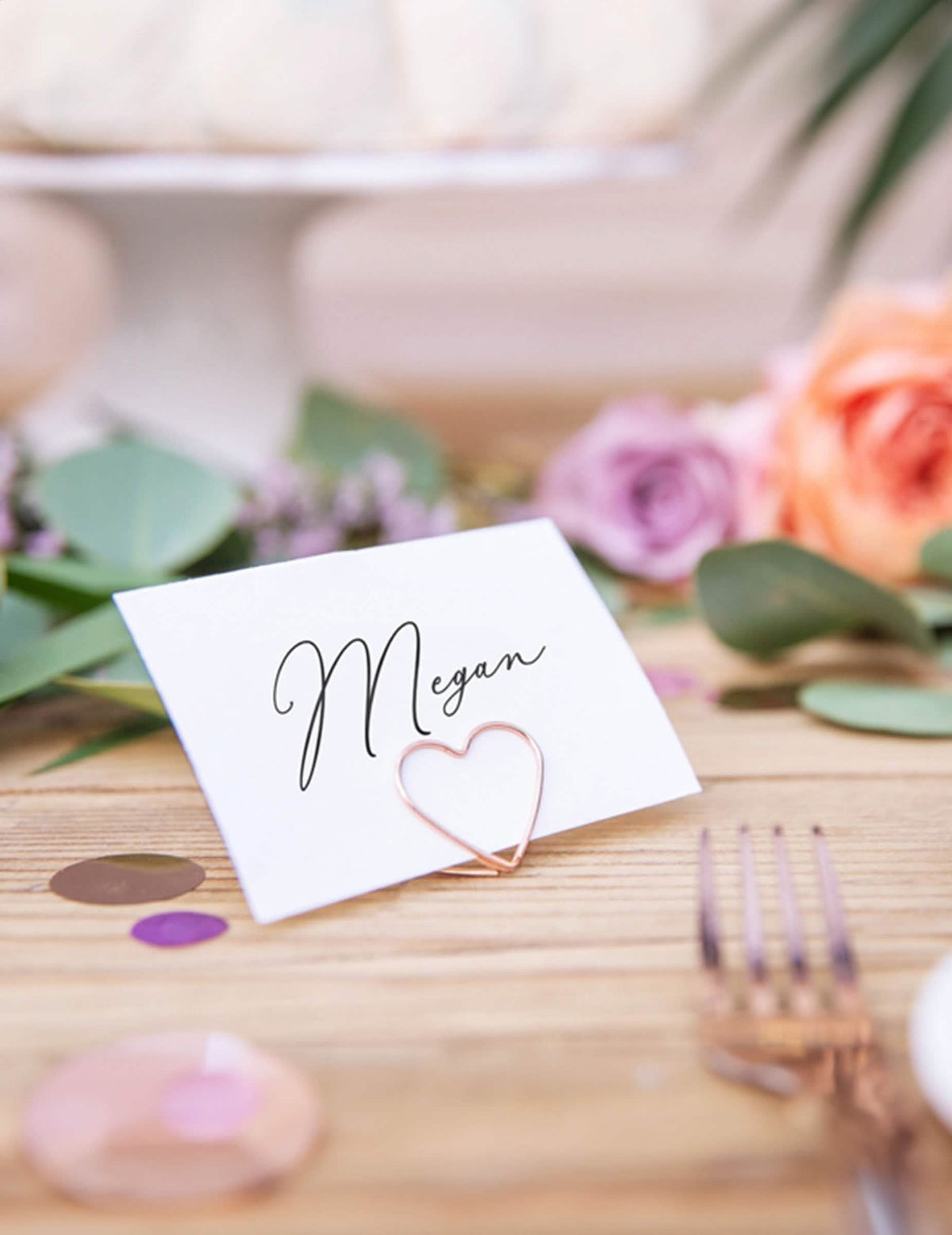 Grande plano de um cartão de convidado segurado pelo marcador de lugar coração para decoração de mesa ouro rosa