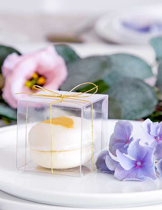 Gros plan sur le macaron et le ruban doré des petites boîtes pour cadeaux pour invités transparentes