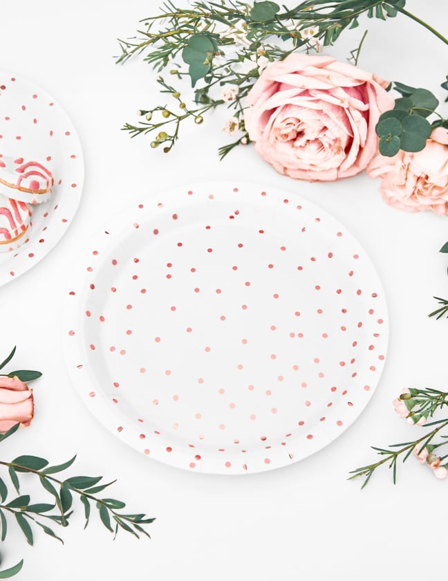 Vista de cima dos pratos de cartão às bolinhas para mesa brancos e ouro rosa