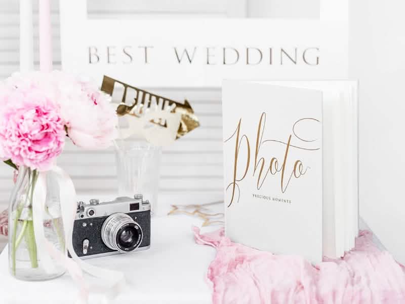 Mise em cena com acessórios e máquina fotográfica do álbum de fotografias de casamento branco e dourado