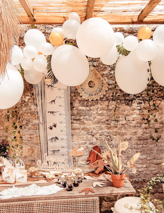 Mise en situation du kit arche de 55 ballons blanche et or avec lierre et feuilles tropicales
