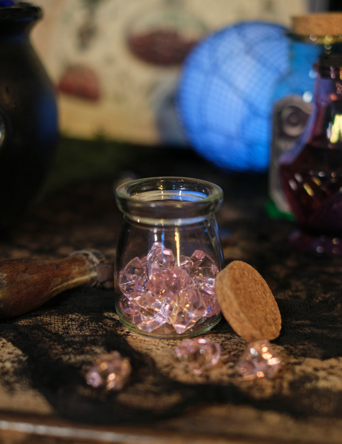 Detalhe dos cristais espalhados em frente ao frasco de pedras efeito cristal para decoração de mesa cor de rosa