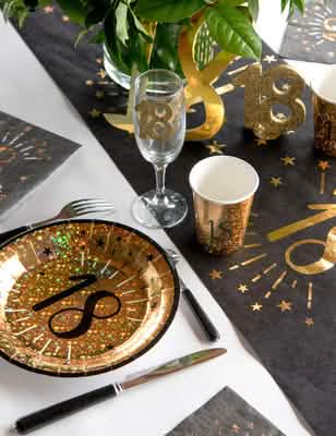 Vista geral de uma mesa de festa com copos de cartão aniversário feliz para festa preto e dourado com motivos de estrelas