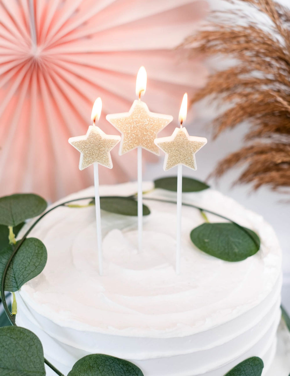 Grande plano das velas acesas sobre um bolo de 3 velas em palitos estrelas para festa