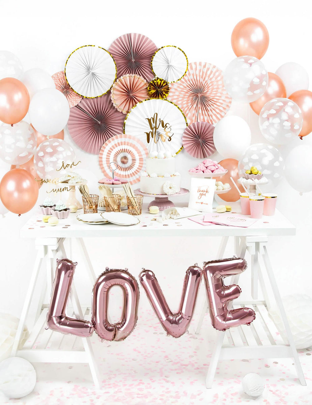 Vista geral sobre uma mesa de festa de 3 rosetas de papel brancas e douradas para decoração