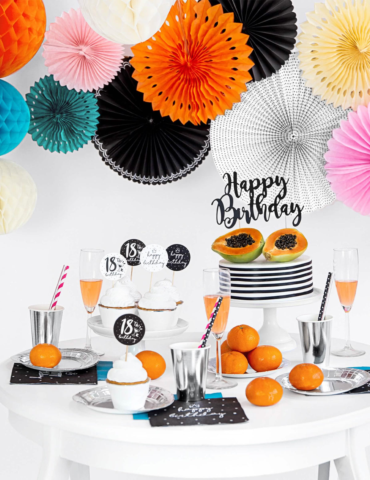 Encenação sobre uma mesa de aniversário de rosetas em papel para decoração, pretas e brancas, com padrões variados