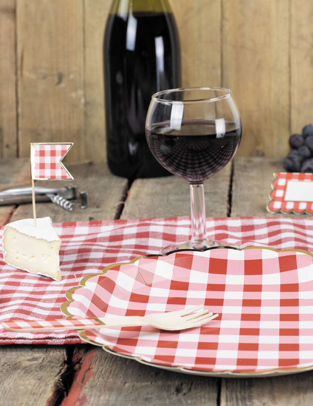 Mise en situation avec verre de vin et fourchette des assiettes festonnées en carton vichy rouge et blanc