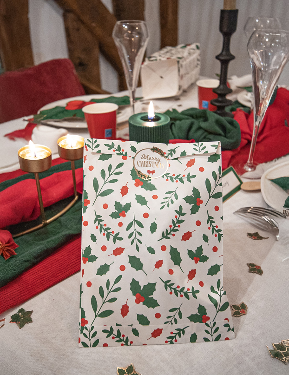 Mise en scène sur une table de fête de la pochette cadeau houx de Noël en papier