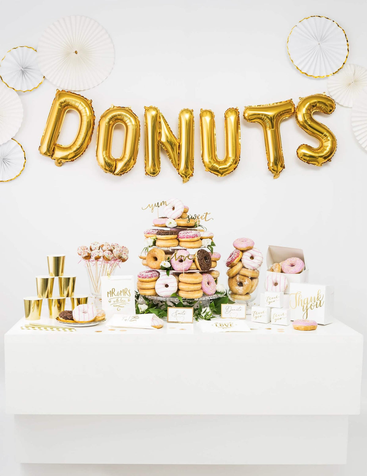 Decoração de candy bar com a palavra DONUTS composta por balão de alumínio dourado com letras