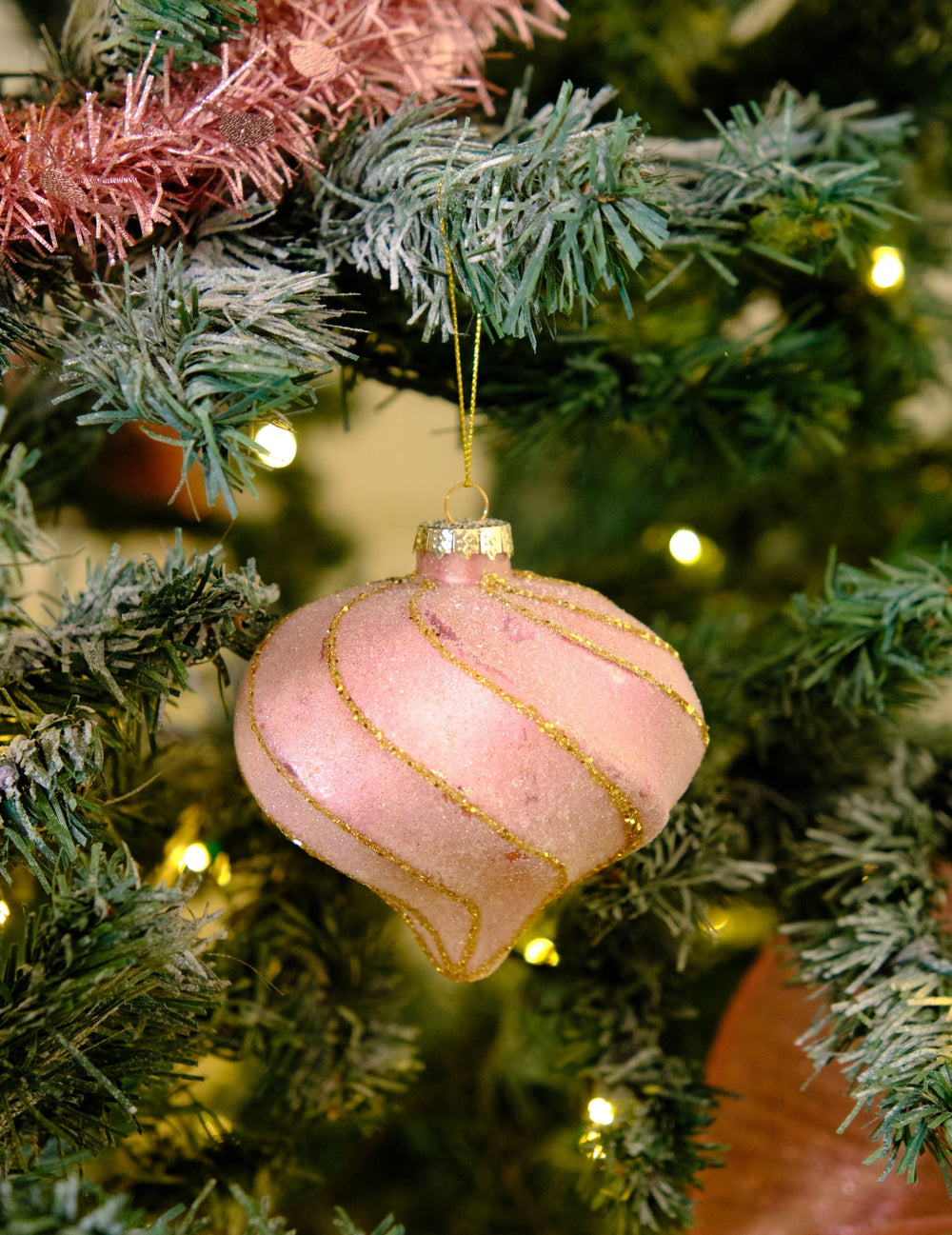 Mise en situation sur un sapin de la boule de noël forme goutte et spirales rose et or pailletée