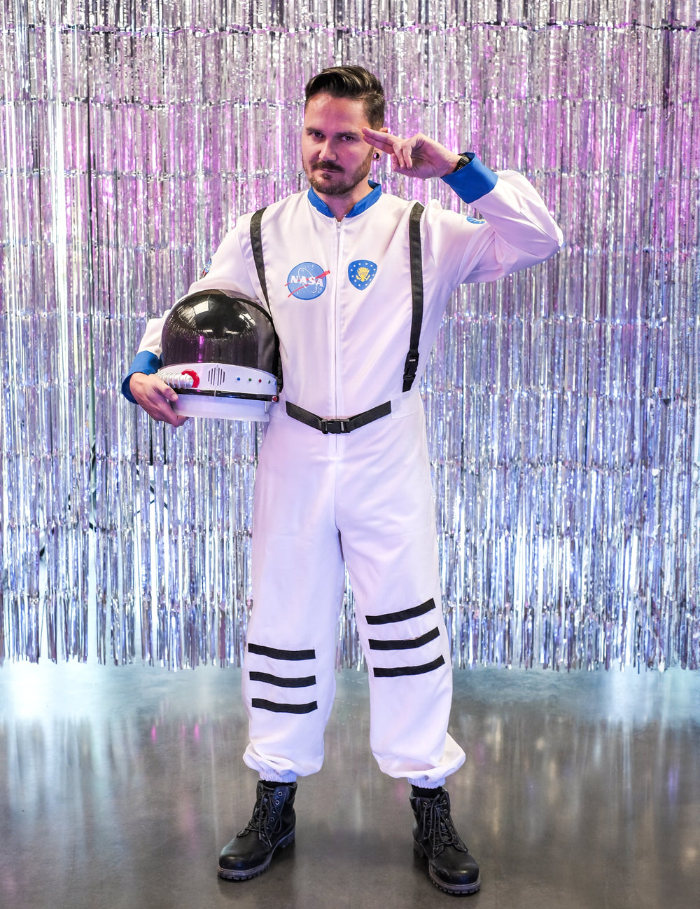 Pose de salut avec casque sous le bras devant un fond argenté du déguisement astronaute de l'espace