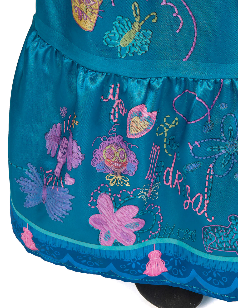 Gros plan sur les pompons et broderies du bas de la jupe du déguisement Mirabel deluxe Encanto™