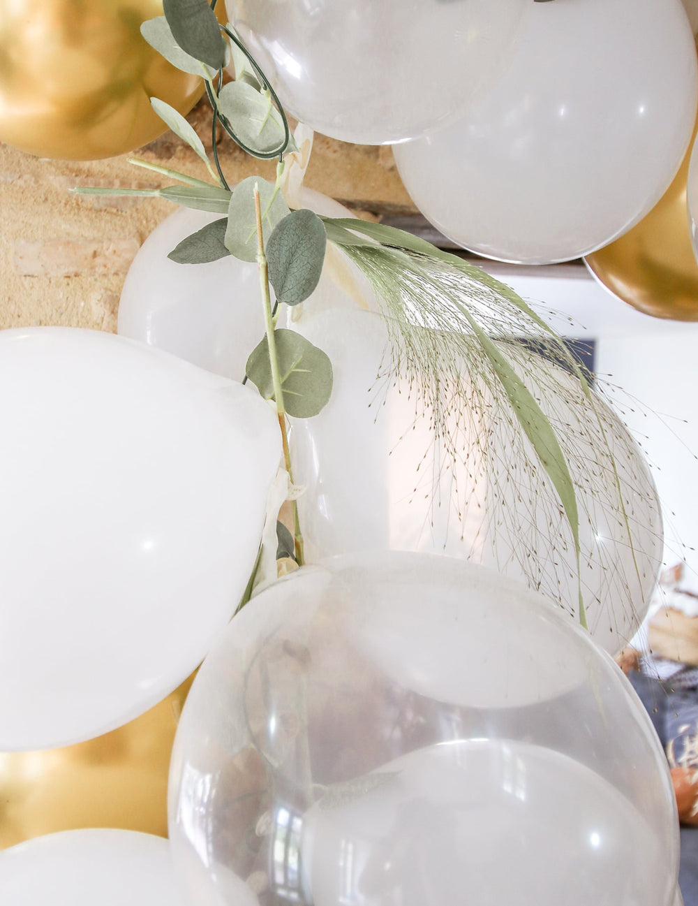 Gros plan sur la décoration végétale du kit arche de 60 ballons blanche et or avec eucalyptus végétale